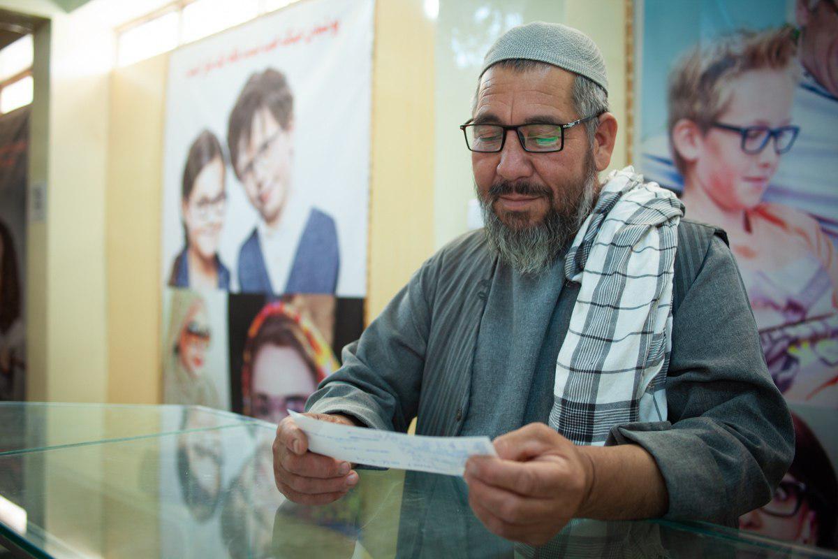 An elder Afghan who has just put on eye glasses and checking his eyesight by reading a note